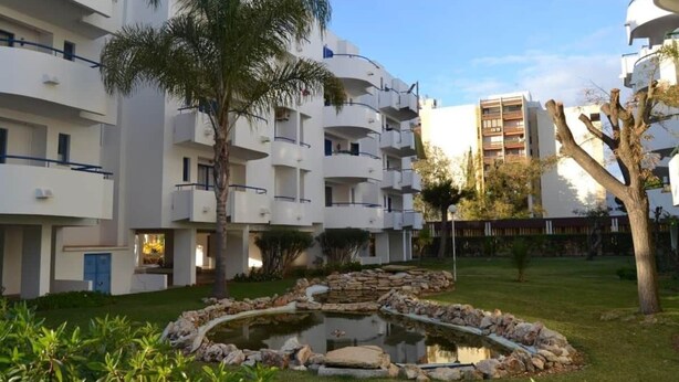 A modern apartment complex with multiple balconies, a central garden with a pond, and surrounding greenery. - Recreational Vehicle (Vilamoura)
