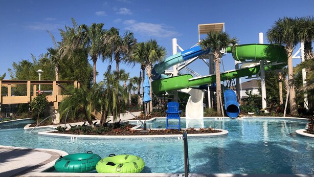 A pool area with a water slide, palm trees, and inflatable rings.