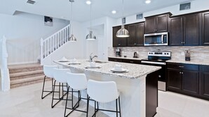 A modern kitchen with dark cabinets, a large island with bar stools, stainless steel appliances, and pendant lighting.