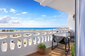 A balcony with a view of the sea, a potted plant, and a chair.