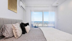 Un dormitorio con cama, sofá, balcón con vistas y aire acondicionado.