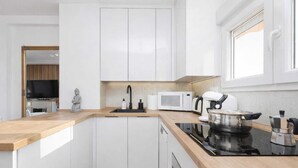Una cocina moderna con armarios blancos, encimera de madera, placa de cocción por inducción negra, microondas y cafetera.