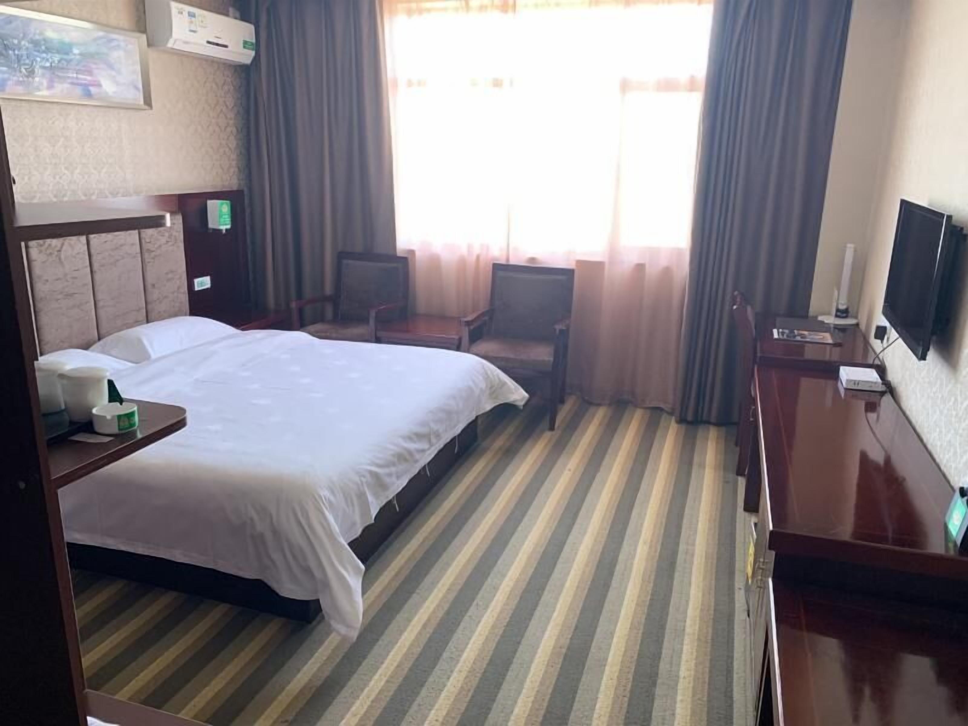 Ein Hotelzimmer mit Bett, Schreibtisch, Sessel, Fernseher und einem fenster mit Vorhängen.