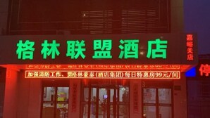 A hotel with a prominent green sign and a red illuminated signboard advertising special offers. - Greentree Alliance Jiayuguan Datang Food Street Sports Avenue Hotel (Jiayuguan)