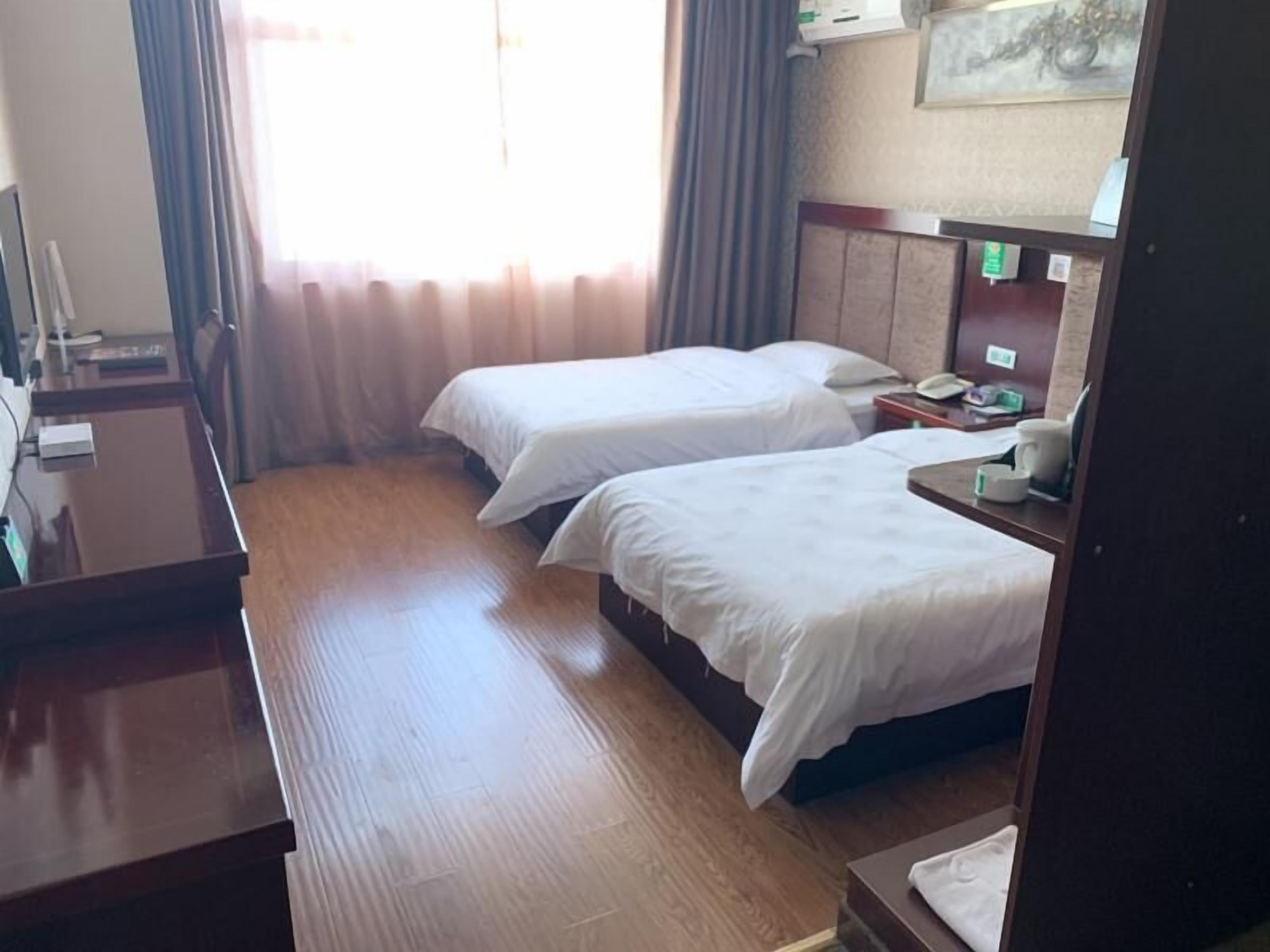A hotel room with two single beds, a wooden desk, a telephone, and a small table with a cup and a book.