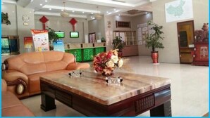 A lobby with a reception desk, a sofa, a coffee table with a vase of flowers, and a large potted plant. - Greentree Alliance Jiayuguan Datang Food Street Sports Avenue Hotel (Jiayuguan)