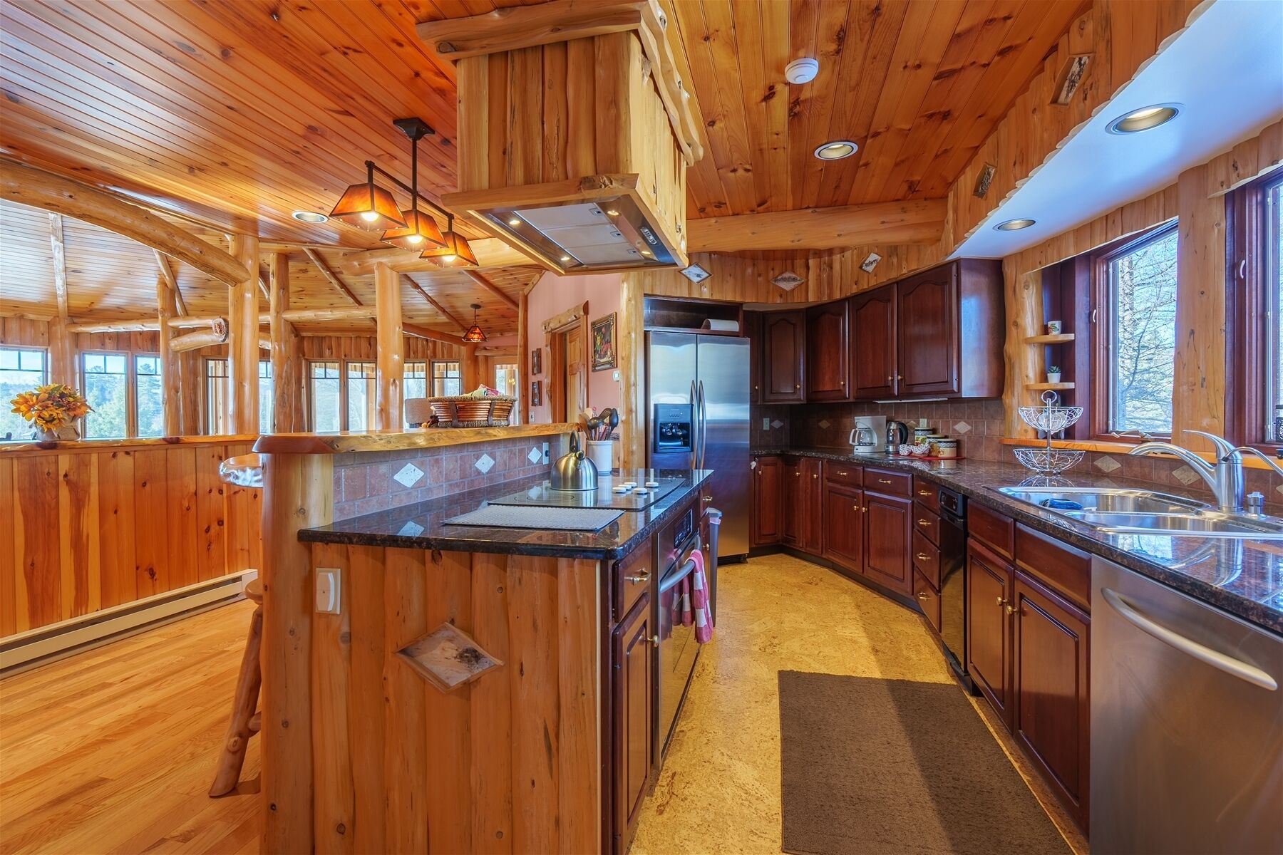 A wooden cabin interior with a kitchen featuring a large refrigerator, wooden cabinets, and a bar area with a sink.