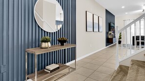 A modern hallway with a wooden console table, a round mirror, and a staircase leading to another level. - Townhome with Star Wars Game Room, Private Pool, PS5 & Themed Bedrooms (Kissimmee)