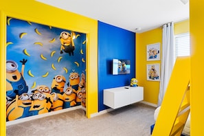 Ein Zimmer mit einem lebendigen Gelb- und Blauton, mit einem Wandgemälde zum Thema Minions und einer weißen Unterhaltungsanlage.