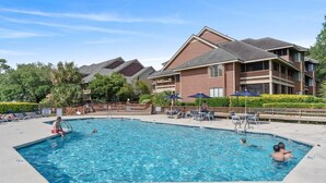A swimming pool with lounge chairs and umbrellas, surrounded by multi-story buildings with balconies.