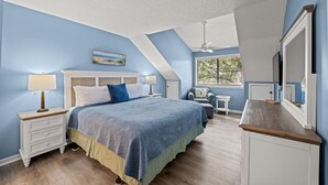 A bedroom with a bed, nightstands, a chair, a small table, a ceiling fan, and a window with blinds.