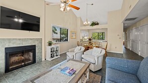 A spacious living room with a fireplace, comfortable seating, a ceiling fan, and a dining area with a view of the outdoors.