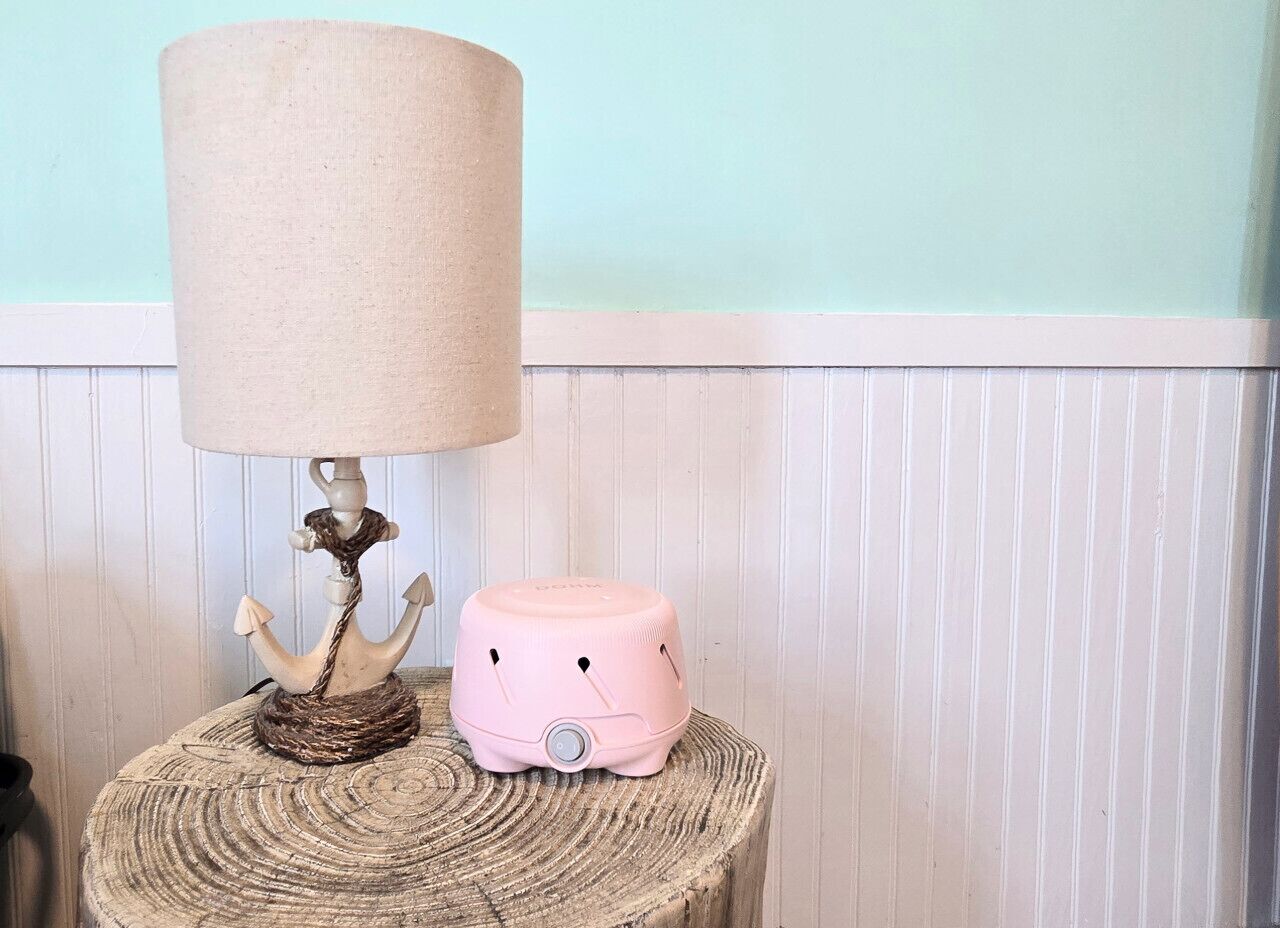 A lamp with a beige shade and a pink object on a round wooden table.