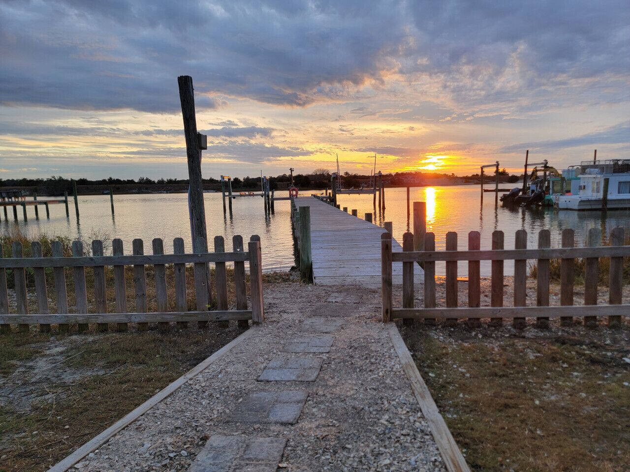 A wooden pathway leading to a dock with a sunset in the background.