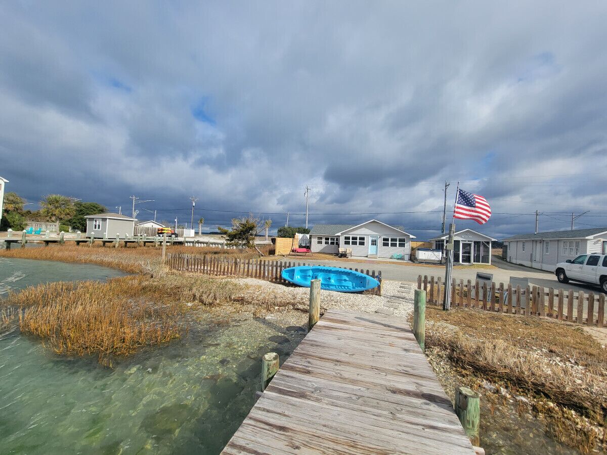 Een houten steiger die leidt naar een blauwe boot, een klein huisje en een Amerikaanse vlag.