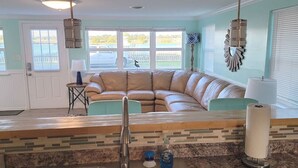 Et køkken med vask, bordplade, hængende lampe og et kig til en beige hjørnesofa i baggrunden.