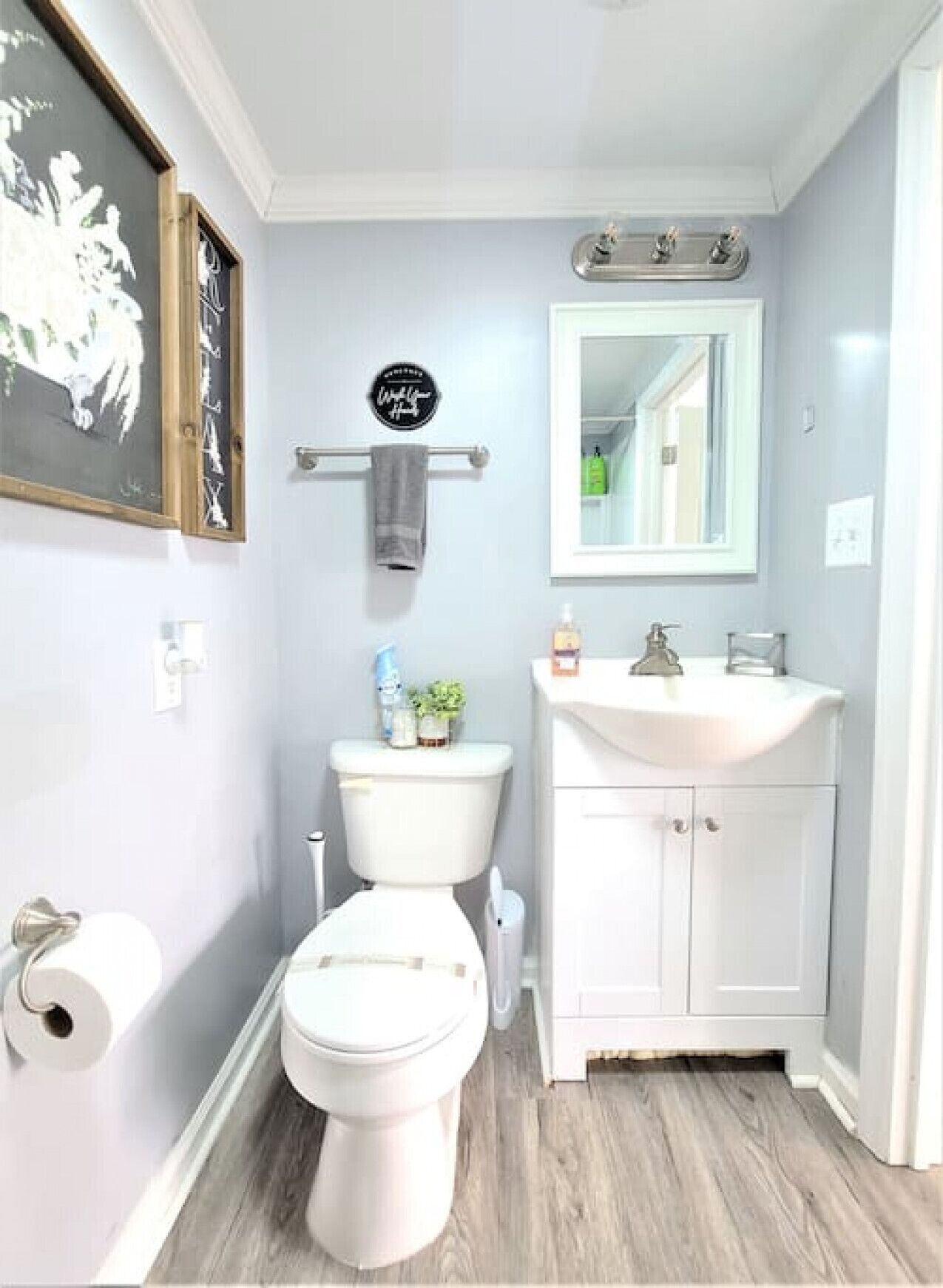 Et badeværelse med toilet, håndvask og et billede i ramme på væggen.
