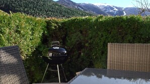 Een terras met rieten meubilair en een barbecue, met uitzicht op een bergachtig landschap.