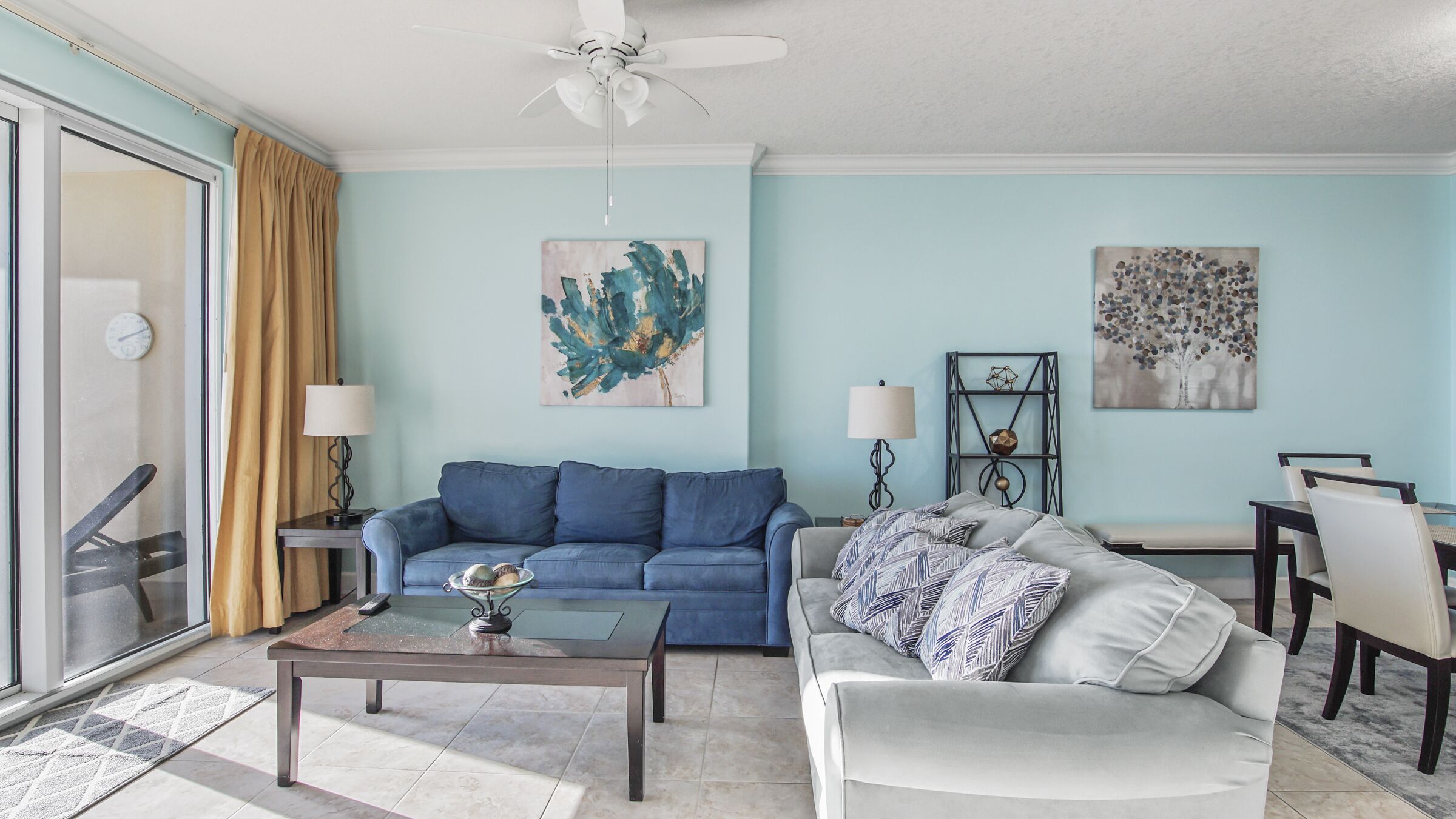 Una sala de estar con un sofá azul, un sillón blanco, una mesa de centro y un comedor con sillas y una mesa.