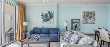 Una sala de estar con un sofá azul, un sillón blanco, una mesa de centro y un comedor con sillas y una mesa.