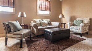 Una sala de estar con sofá, sillón, reposapiés y dos lámparas.
