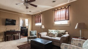 Una sala de estar con sofá, sillón, reposapiés y televisor sobre un mueble.