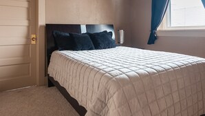 Una cama bien hecha con un edredón acolchado color beige, un cabecero oscuro y dos almohadas oscuras.