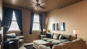 Una sala de estar con un sofá color beige, un televisor de pantalla plana, un ventilador de techo y tres lámparas de pared.