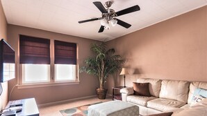 Een woonkamer met een plafondventilator, een grote potplant, een bank, een kleine tafel en een lamp.