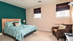 Een slaapkamer met een bed, een stoel en twee ramen met jaloezieën.