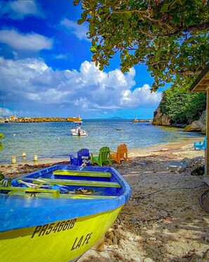 Una playa con un bote, sillas coloridas y un litoral rocoso.