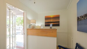 A reception area with a wooden counter, a lamp, and a sunset painting on the wall. - Bluff Shoal Motel (Ocracoke)