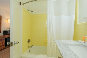 A bathroom with a bathtub, yellow tiles, a white shower curtain, and a marble countertop. - Bluff Shoal Motel (Ocracoke)
