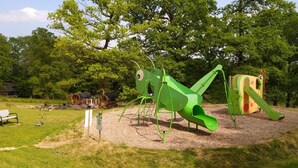 A playground with a green slide and climbing structures, surrounded by trees and a picnic area. - GITE D'OBSERVATION (4/6 pers) - Stopover in the forest (Noues de Sienne)