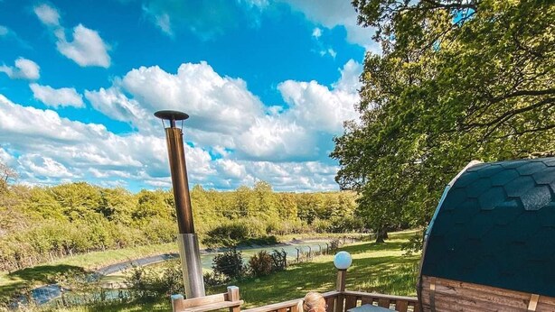 A hot tub on a wooden deck with a view of a lake and trees.