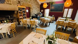 A restaurant with multiple tables set for dining, a stone wall, a fireplace, and a bar area.
