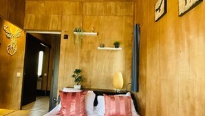 Een slaapkamer met een houten wand, een bed met roze en witte beddengoed, een kleine potplant en een plank met decoratieve spullen.