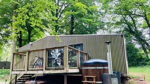 A wooden cabin with a large window, a wooden deck, and a hot tub. - BUNGALOW TERRACE (3pers) with private hot TUB - Forest stopover (NOUES DE SIENNE)