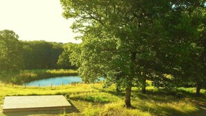 A serene outdoor setting with a wooden deck, a pond, and lush greenery. - BUNGALOW TERRACE (3pers) with private hot TUB - Forest stopover (NOUES DE SIENNE)