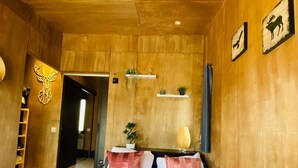 A bedroom with a wooden ceiling, a bed with white and pink bedding, a bedside table with a lamp, and a wall-mounted shelf with plants. - BUNGALOW TERRACE (3pers) with private hot TUB - Forest stopover (NOUES DE SIENNE)