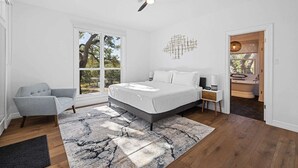 Ein modernes Schlafzimmer mit einem großen Bett, einem Deckenventilator, einem Fenster mit Aussicht und einem durch eine offene Tür erreichbaren Badezimmer.