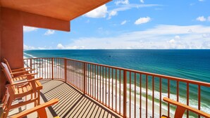 Ein Balkon mit Holzkubeln blickt auf einen Strand mit klarem, blauem Wasser und sandigem Ufer.