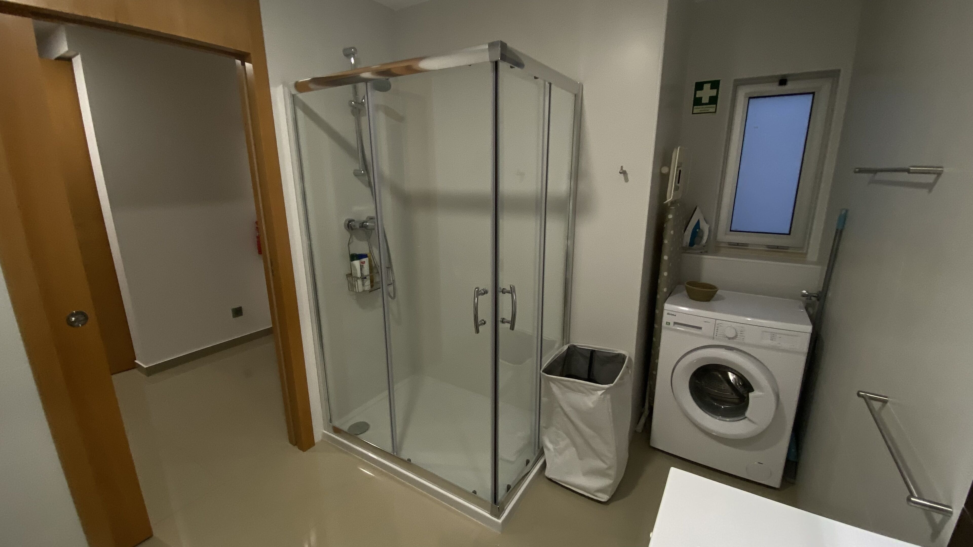 Un bany amb dutxa trencada per vidre, rentadora i una finestra petita.