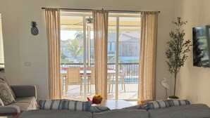 Un salon avec un grand canapé gris, une table à manger avec des chaises, un ventilateur de plafond et une vue sur le balcon extérieur.