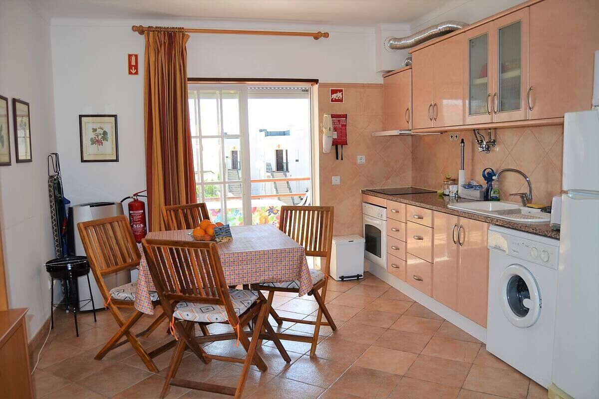 A compact kitchen with wooden cabinets, a washing machine, and a dining table with chairs.