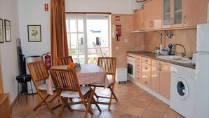A compact kitchen with wooden cabinets, a washing machine, and a dining table with chairs. - Altura T1 Algarve Sun + Beach (Altura)