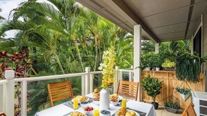 A dining area with a table set for breakfast, surrounded by lush tropical plants and a wooden fence. - Wailea Luxury Retreat | Walk to Beach & Shops (Wailea-Makena)