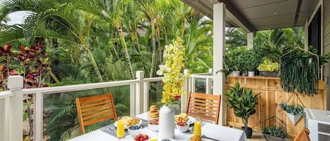 A dining area with a table set for breakfast, surrounded by lush tropical plants and a wooden fence.