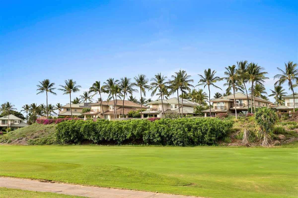 A golf course with a well-maintained green, surrounded by palm trees and residential buildings in the background.