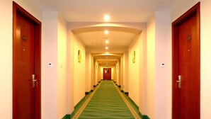 A hotel hallway with a green carpet, wooden doors, and a light-colored ceiling. - Greentree Inn Qinhuangdao Changli County Railway S (Qinhuangdao)